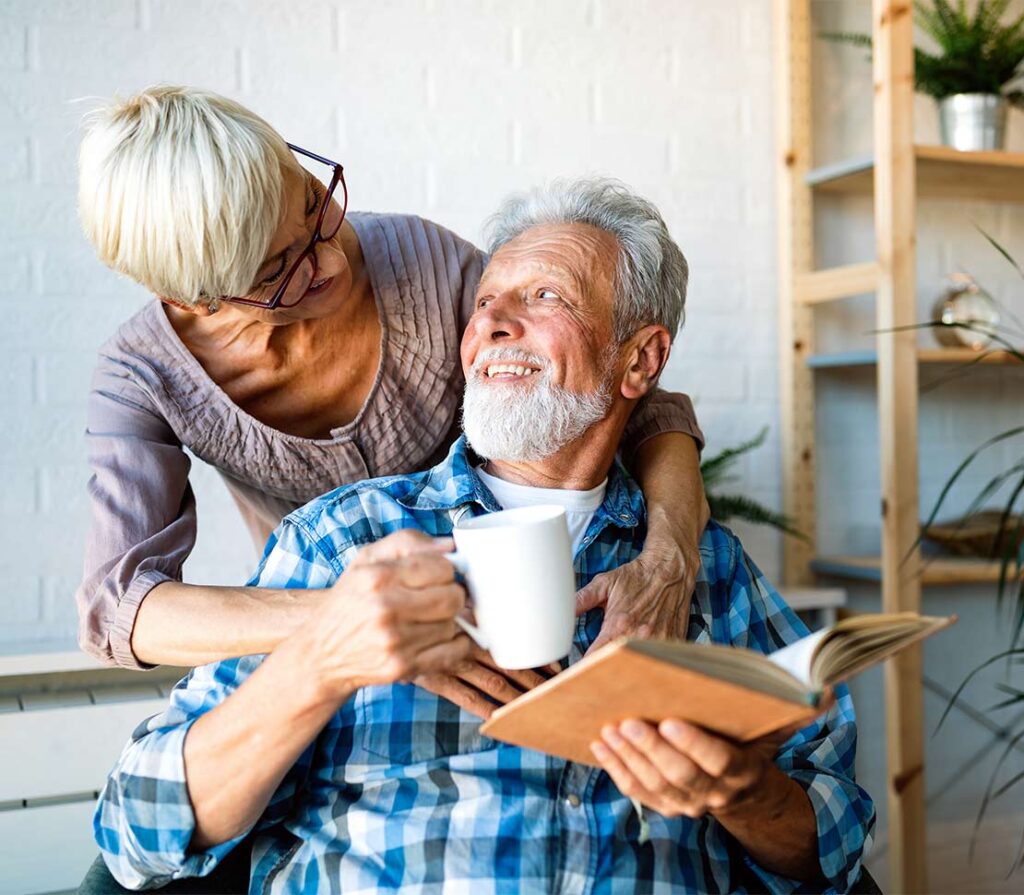woman hugging her husband while he reads a book and drinks coffee how much money do you need to retire comfortably houston tx